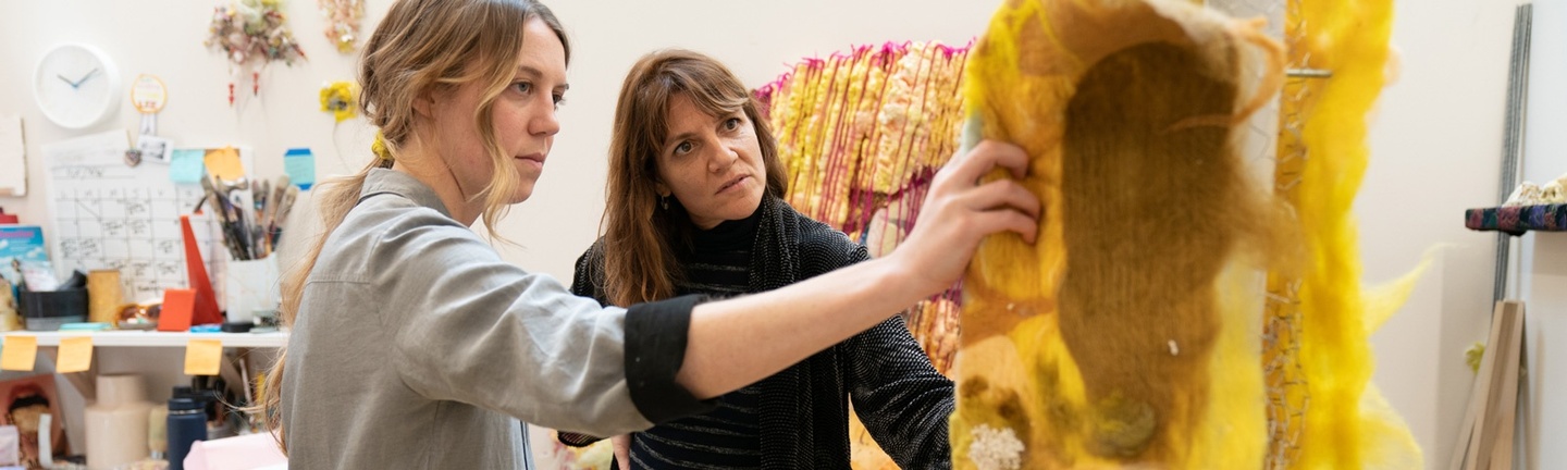 Two people look at a construction of yellow felt in an artist's studio.