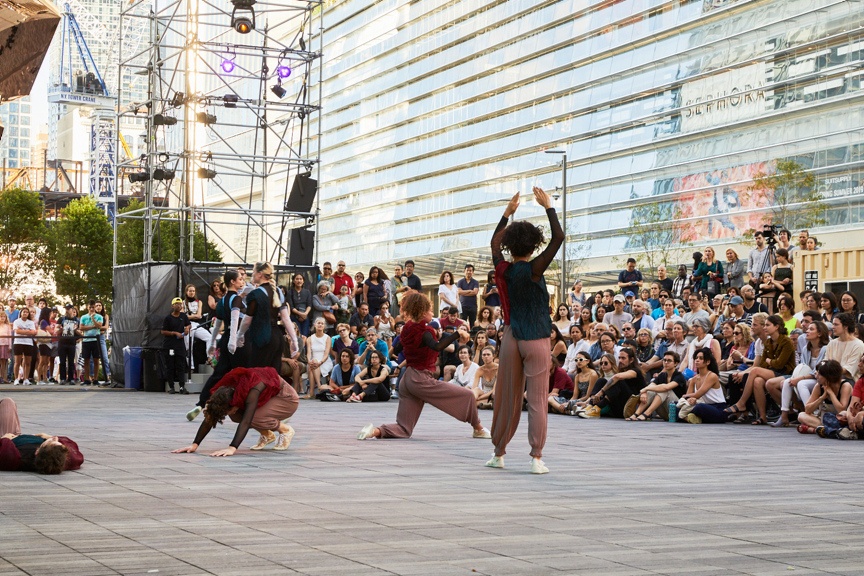 Four dancers in motion on an outdoor stage.