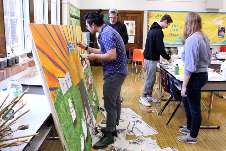 People work on a large canvas painting in an elementary school classroom.