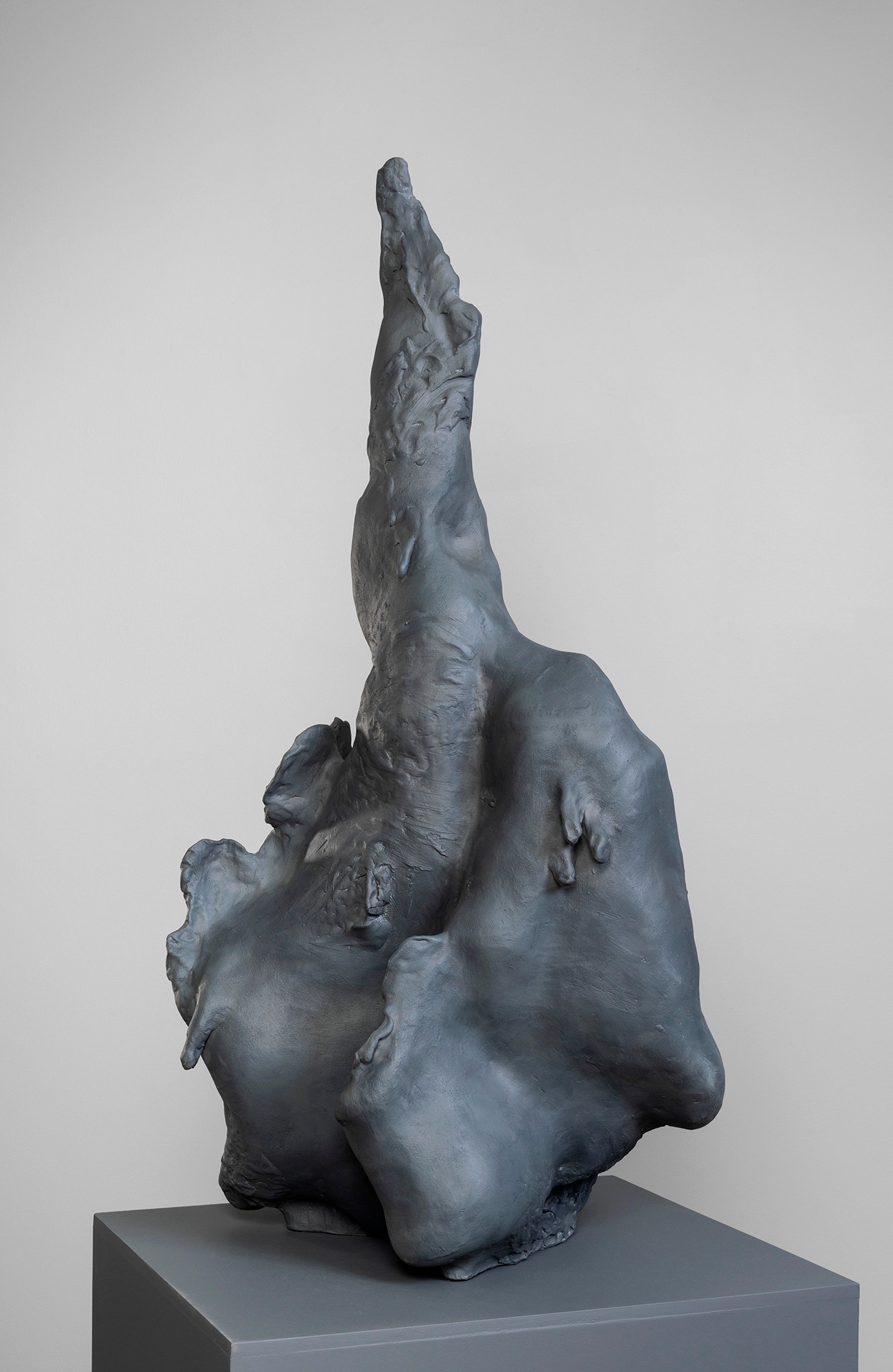 A dark, vaguely amorphous sculpture on a dark gray platform. The sculpture's forms come to a point at the top.