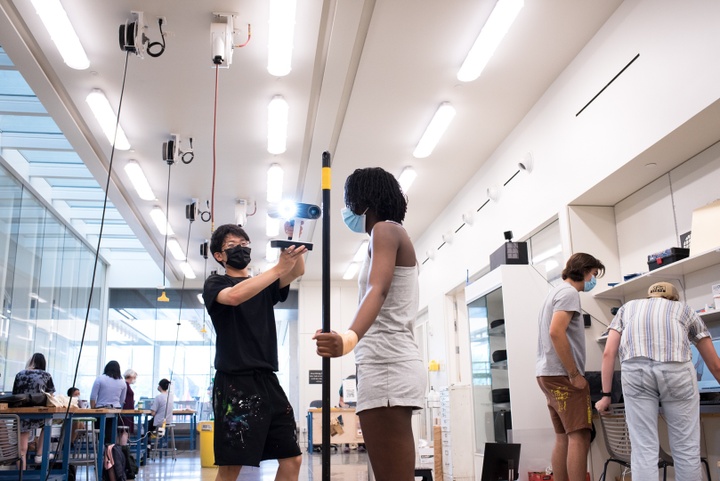 Low angle shot of a person aiming a 3D scanning device at another's head.