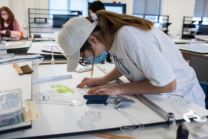 Person leans over a drafting table to work on a drawing using French curves.