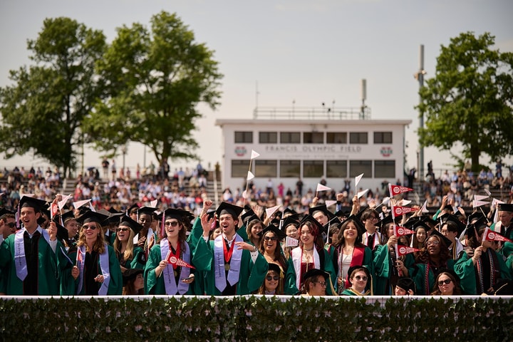 A crowd of university graduates wearing regalia cheer