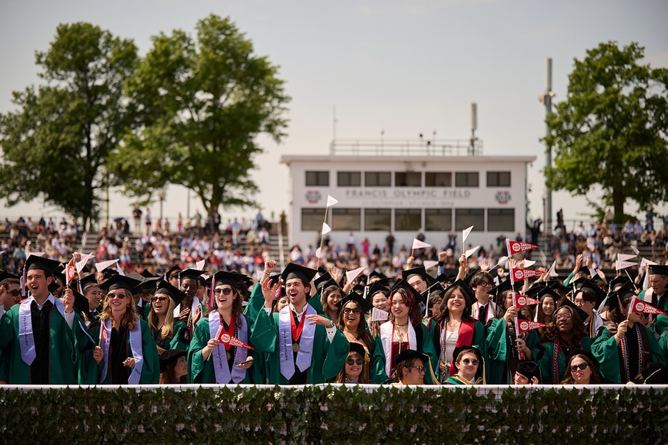 A crowd of university graduates wearing regalia cheer