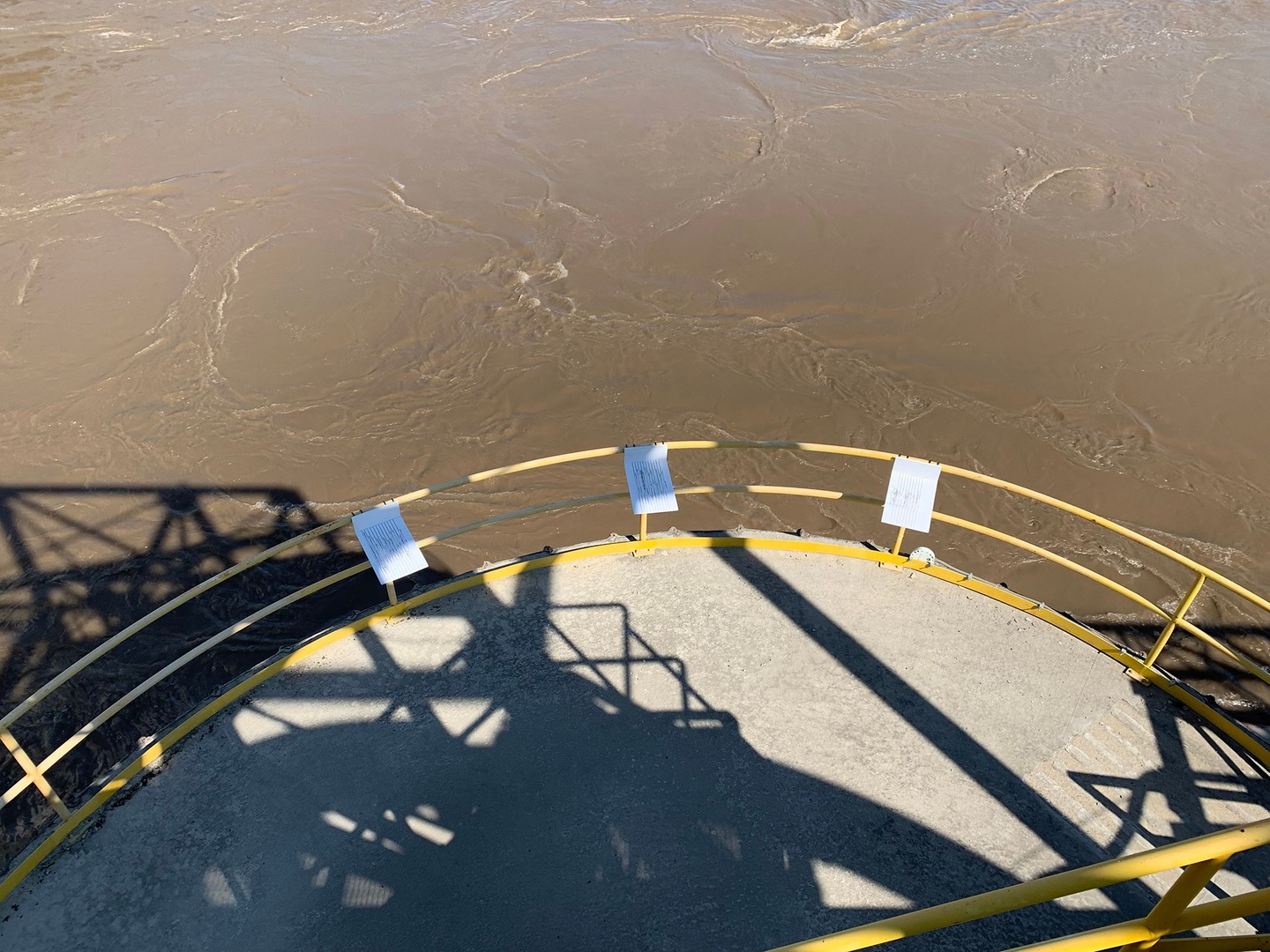 Viewing platform on top of a body of water. On the yellow railings of the platform there are 3 L shaped sculptures with lines hanging off it