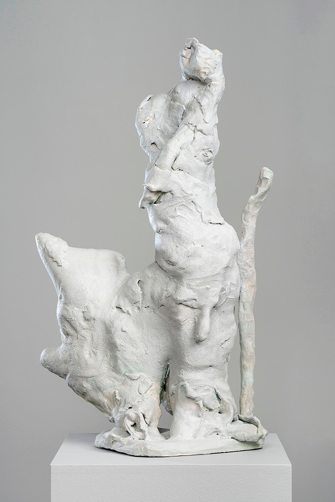 A white sculpture on a white platform: while unidentifiable in form, its cracks, folds, and protrusions are vaguely organic, with a branch-like portion extending upwards from the side.
