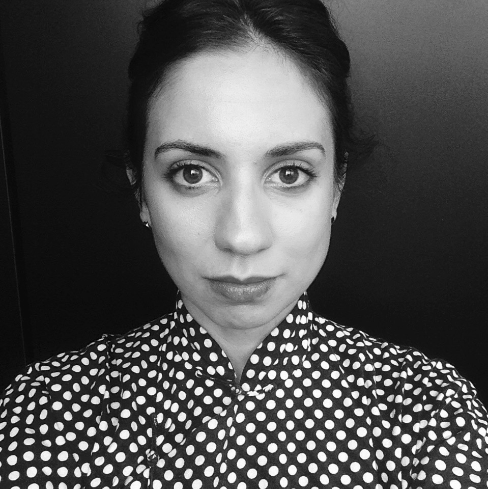 A black-and-white photo of Sophia Marisa Lucas. She looks into the camera in the close-up image and wears a white polka dotted shirt. 