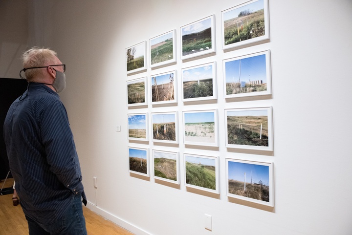 A gallery visitor stands in front of 16 photographs arranged 4 by 4 in a gallery