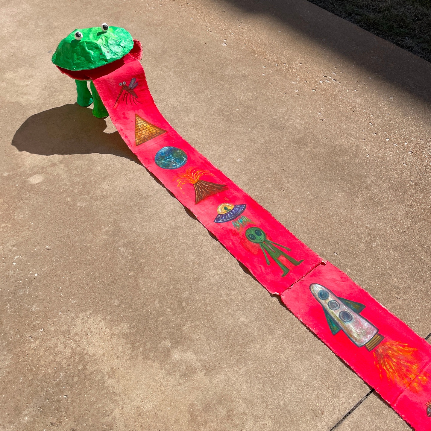 A sculpture of a frog with a very long, red tongue with insects painted on it. 