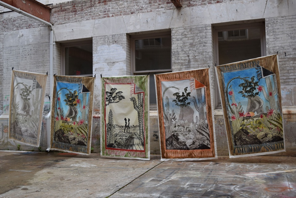 5 large final Paula Wilson prints hang to dry on a clothesline. The prints differ in color and feature cacti, figures sitting under an umbrella and a butt in the center.