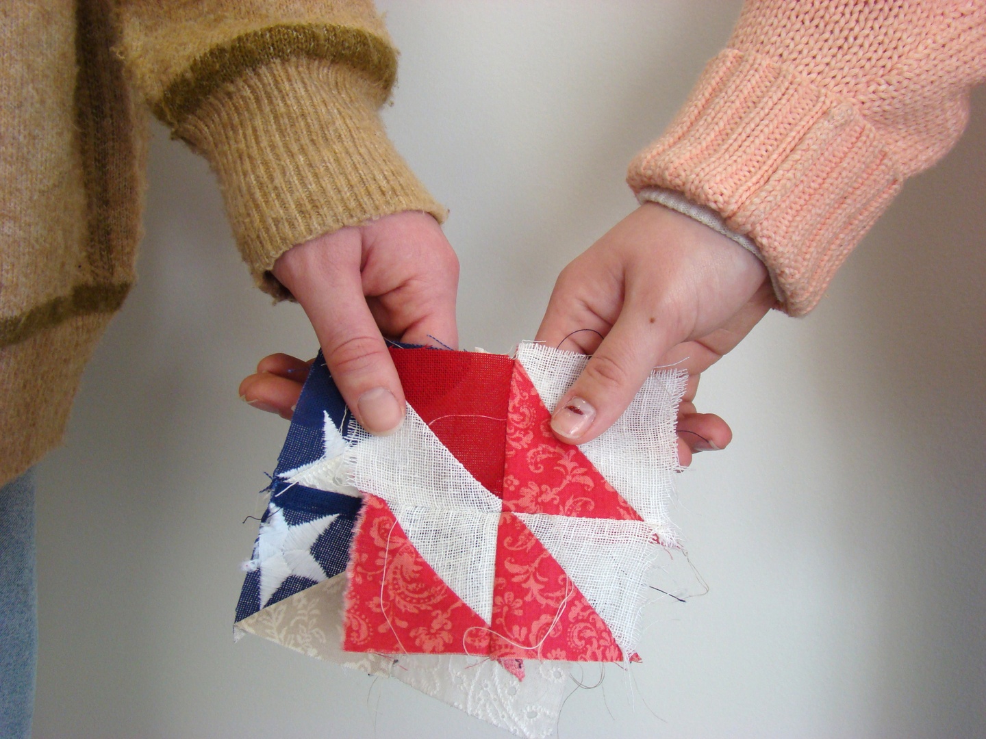 Photo of two different people's hands jointly holding fabric squares that together resemble elements of the American flag.