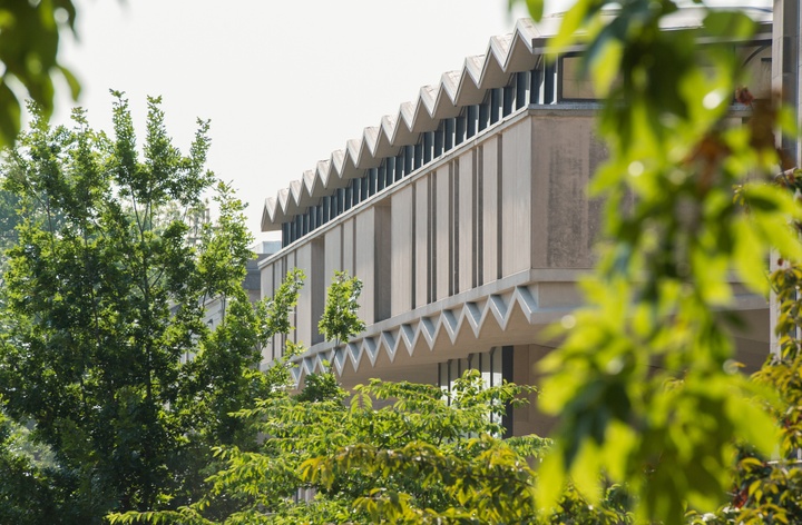 View of a midcentury style building with a pleated roof seen through spring foliage.