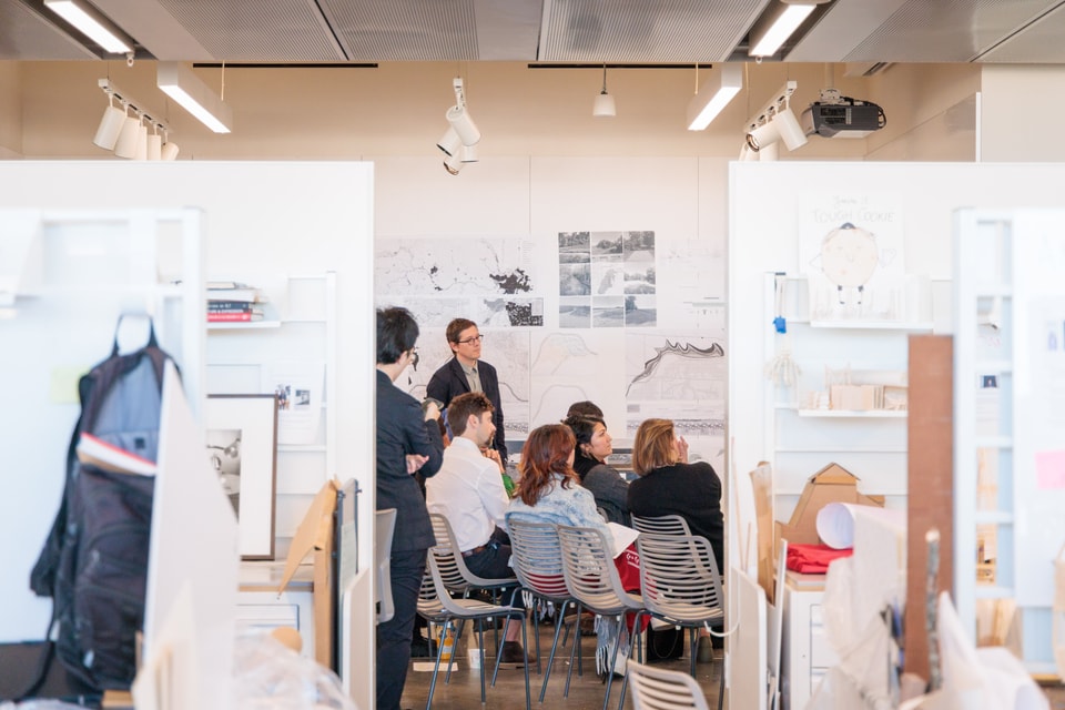 several students in an landscape architecture review in a gallery with white walls and designs pinned up