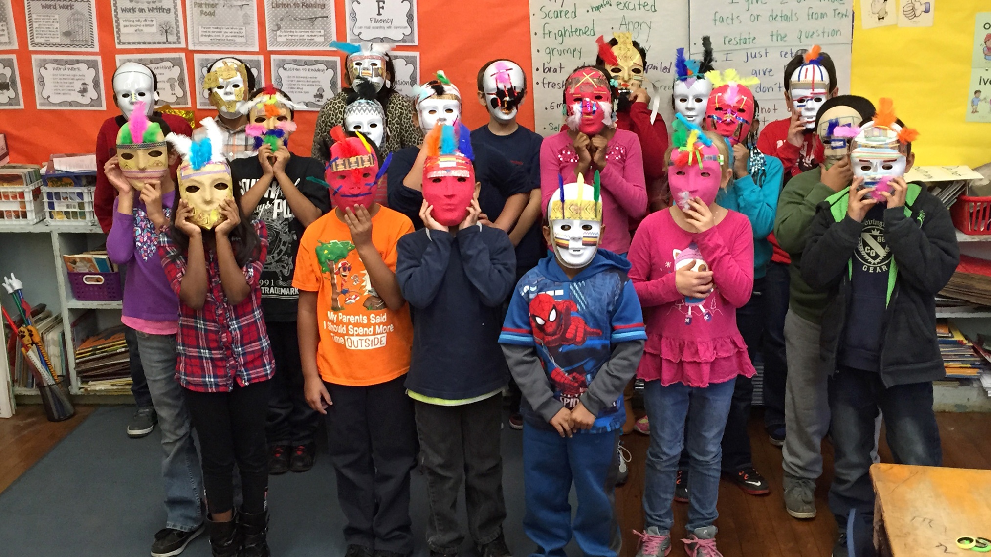 A group of children wearing colorful, handmade masks in front of an orange and yellow wall.