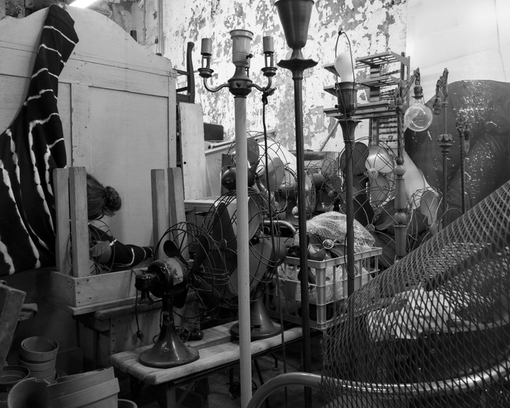 Black and white image of a collection of old fans, lamps, and other items. 