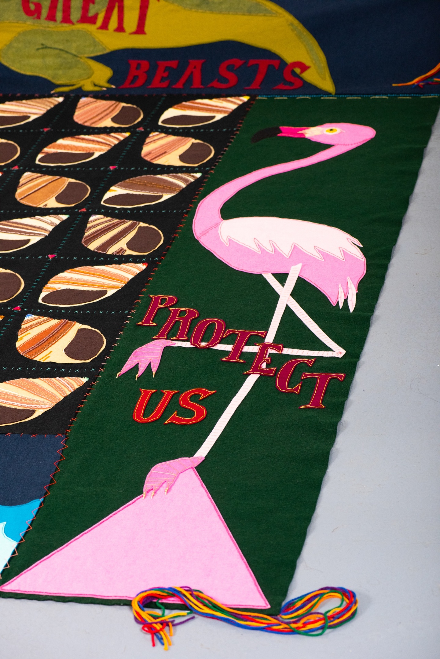 Detail of the bottom right corner of the quilt, which depicts a flamingo standing one-legged on top of a large pink triangle with the words "Protect Us" around it.