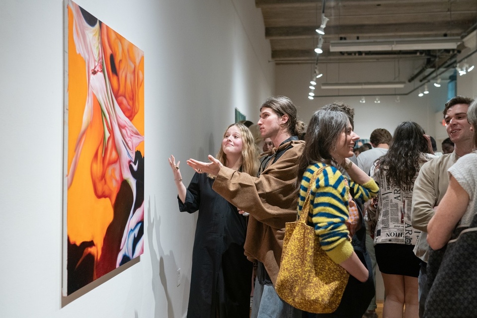 Two students gesture with open palms and comically distinguished expressions at a brightly colored painting in a gallery.