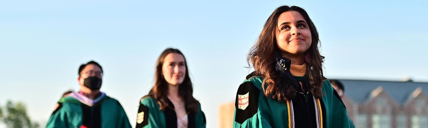 Three people in commencement regalia walk in a line