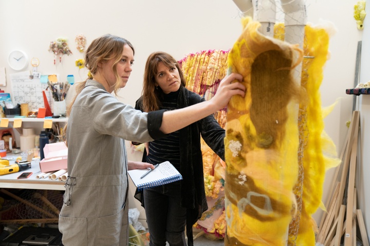 Two people look at a construction of yellow felt in an artist's studio.