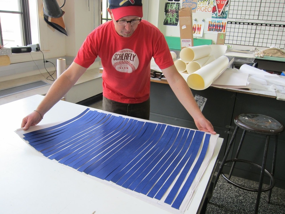 A person places a large sheet of paper with blue strips of paper arranged horizontally through it like stripes