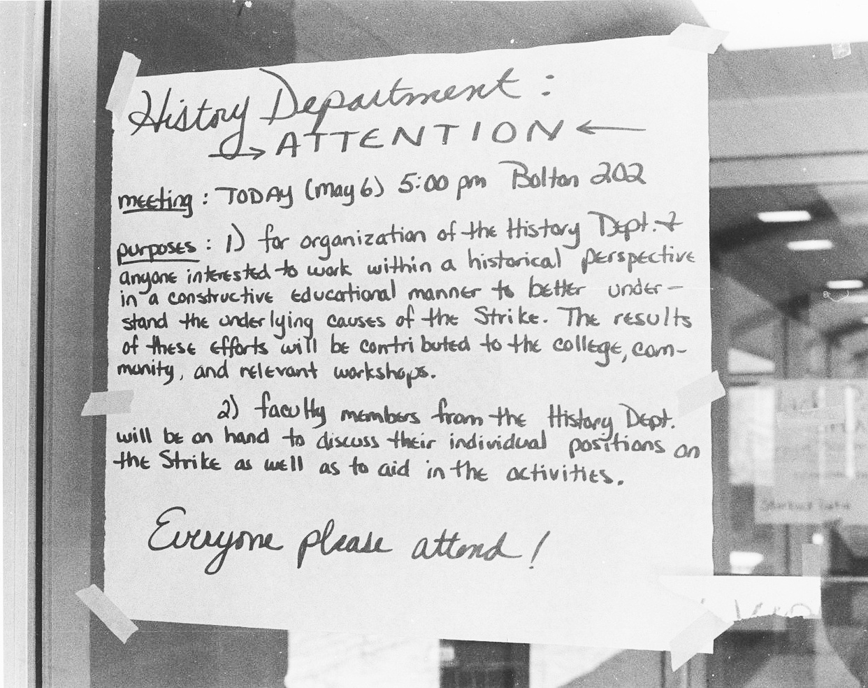 A black and white photograph shows a handwritten sign labelled “History Department: ATTENTION” with details about a meeting taped to a glass window or door.