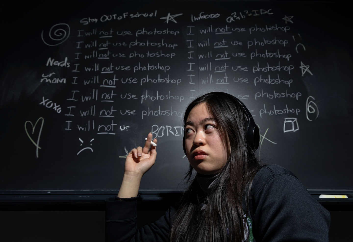 A photo of a person in front of a chalkboard with the text "I will not use photoshop" written several times.