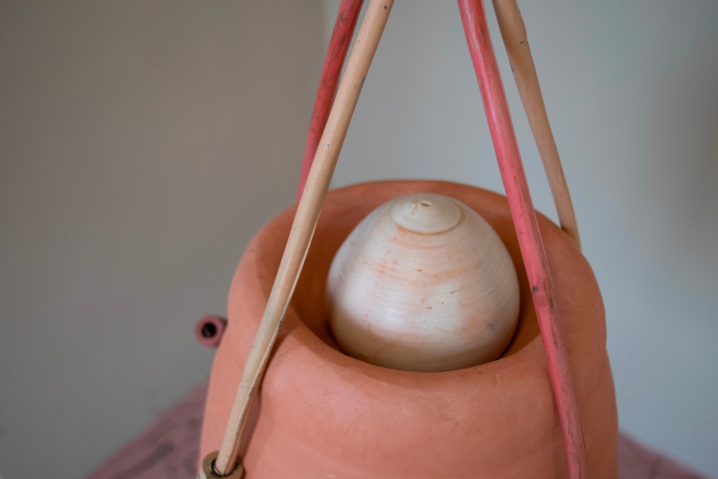 detail of a sculpture of a hanging jar made from ceramics in terracotta, reds, and tans