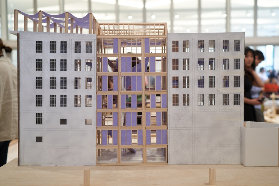 Closeup of architectural model in three sections - 1.) 7 story concrete block with a rooftop deck covered by purple sunshades, 2.) 7 story wooden block with open floorplan and purple panels in the windows, and 3.) a third concrete block section.
