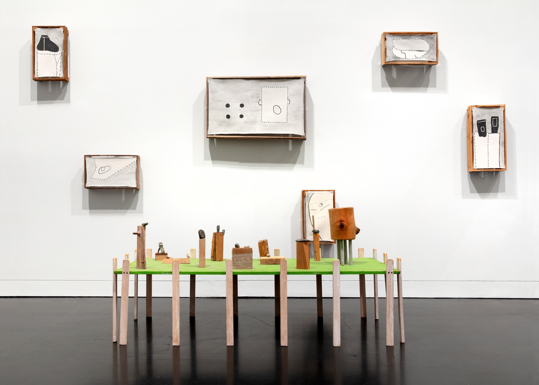 A sculptural artwork by artist Ree Morton which includes mounted parts as well as a green table-like structure with small pieces sitting on top. The artwork is made of acrylic paint on canvas mounted on wood, wood, acrylic paint, and stones