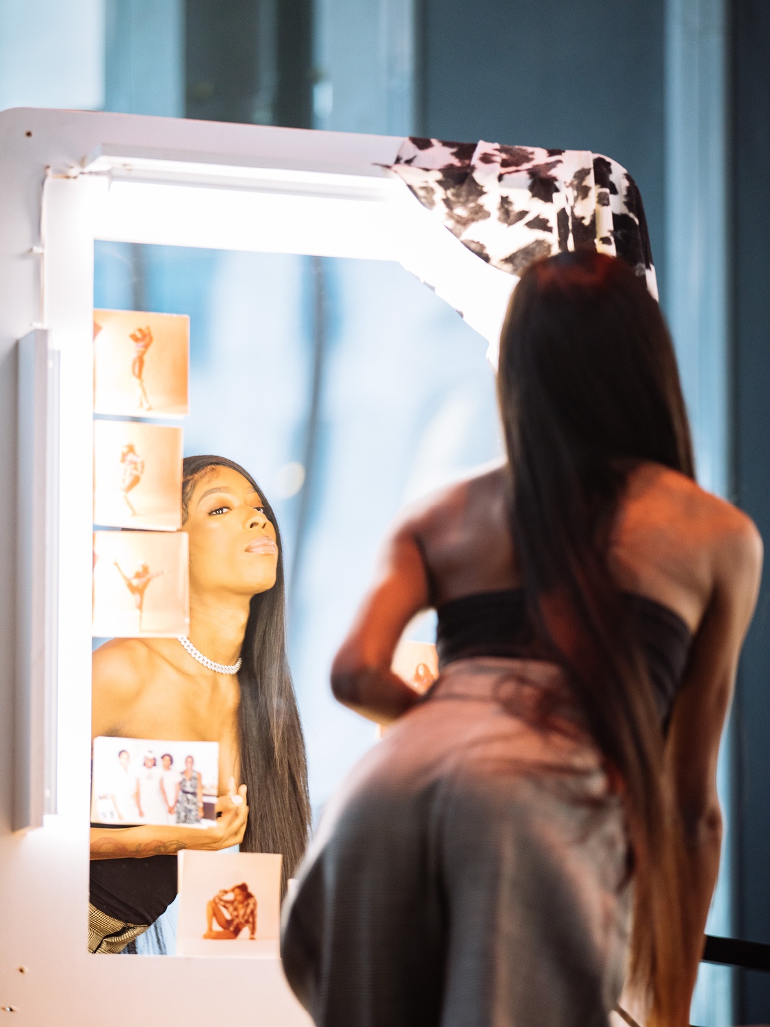A woman looks into a dressing room mirror with photos attached to its frame. 