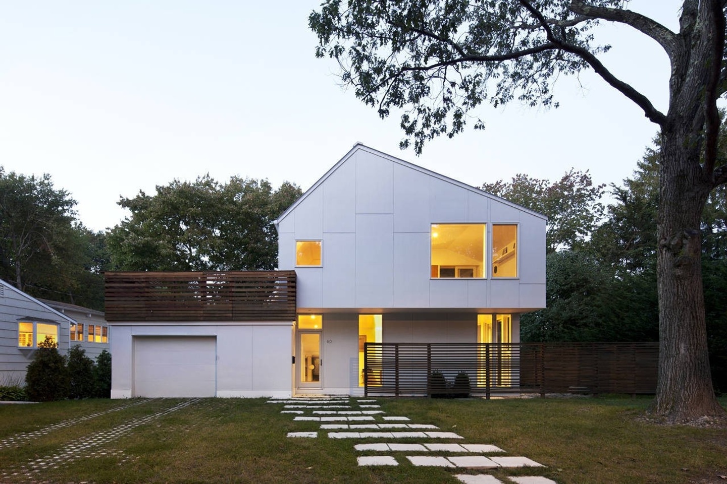 White, two-story structure at dusk with interior lights on