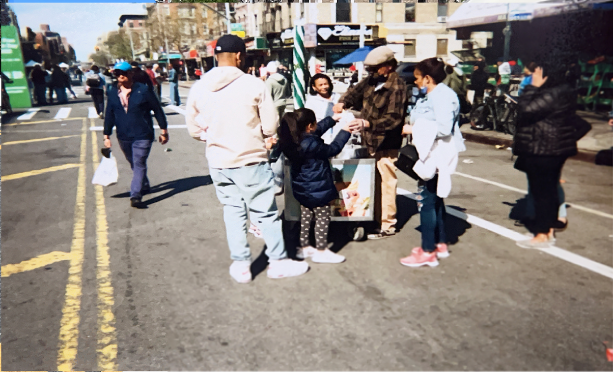 A family of four gathers around a street vendor in the middle of a NYC street during a street fair. 