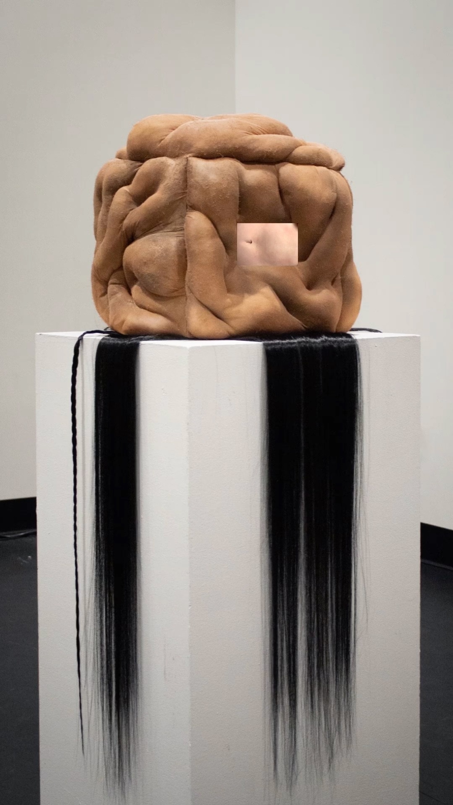 A cube made of humaneque body parts with hair cascading down the stand.