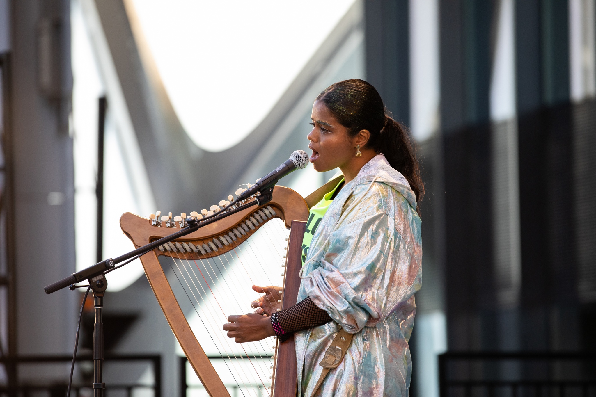Performer singing and playing harp on outdoor stage.