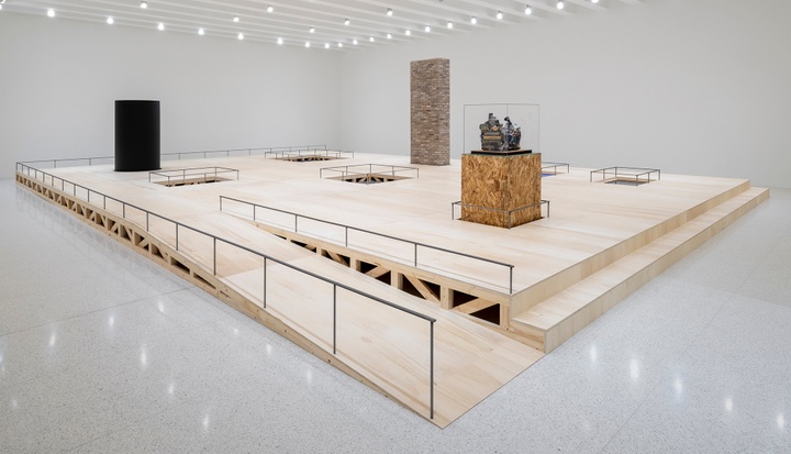 A gallery installation of a wood platform, on which are placed various sculptures