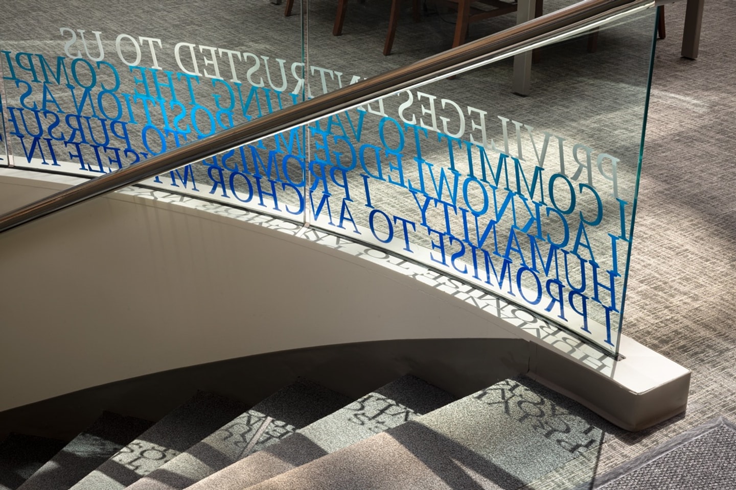 Detail photo of blue text vinyl on a glass half-wall along a staircase with the hippocratic oath