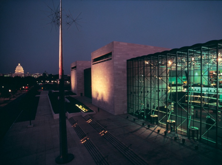 Nighttime photo of the exterior of the museum, with a glass facade lit greenish to the right.
