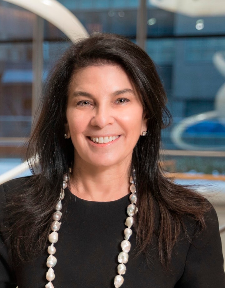 headshot of a woman with shoulder length dark hair wearing a black shirt with a long necklace