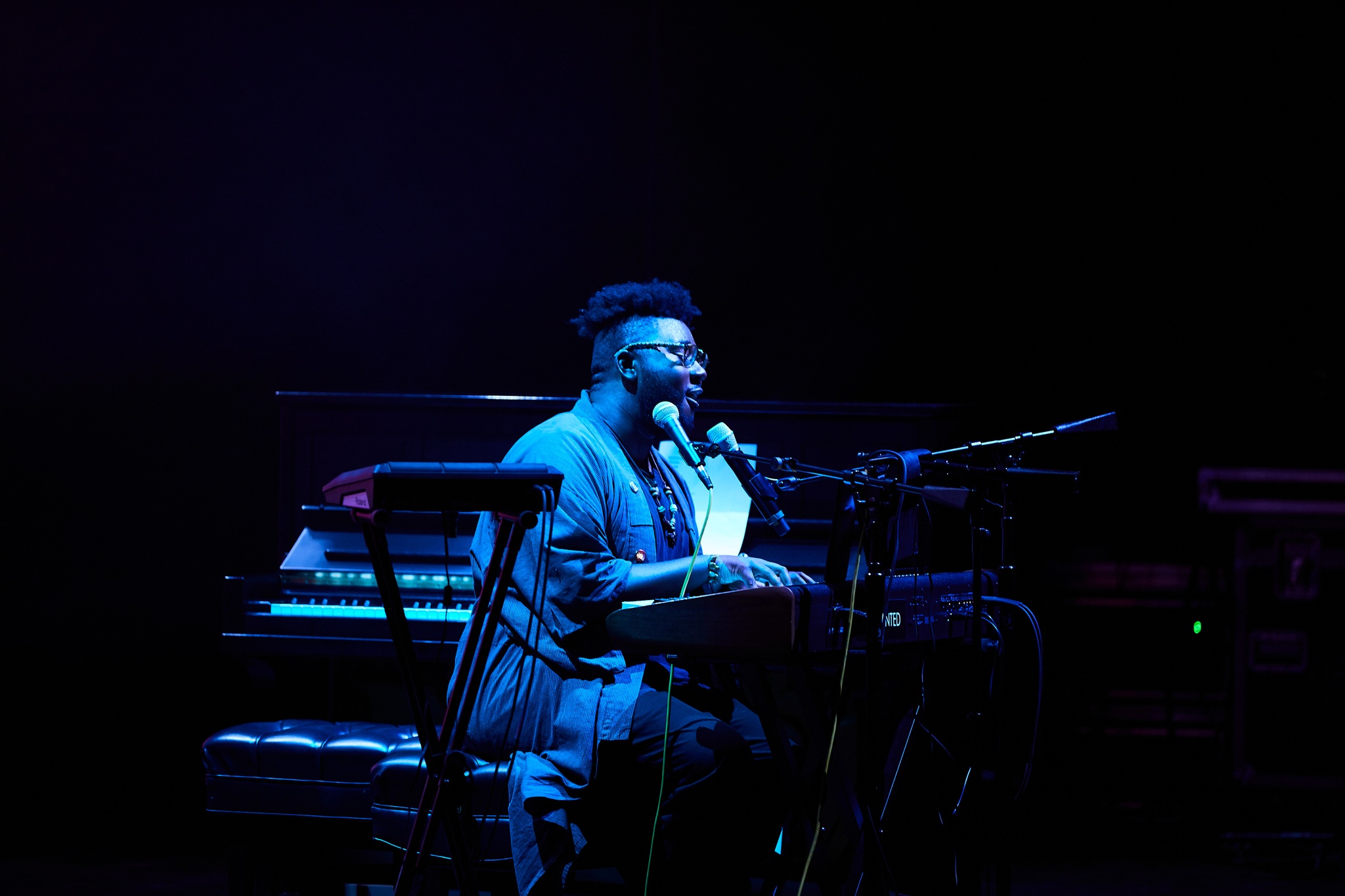 Tariq playing piano while singing on blue-lit stage.