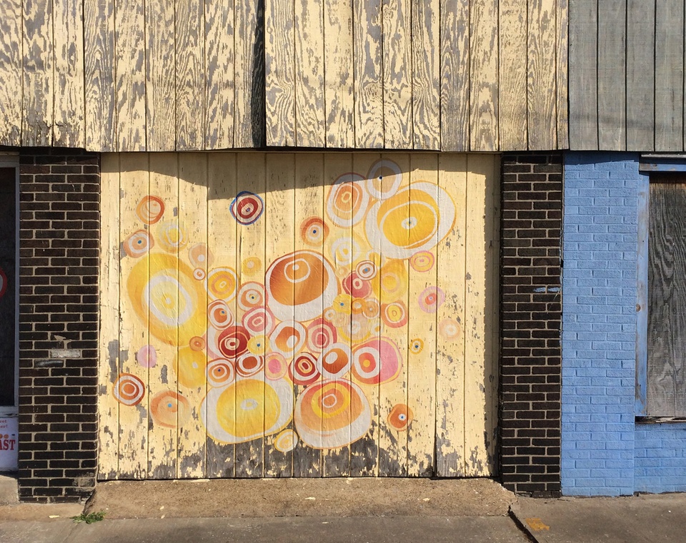 Light colored wooden planks in front of a building with circular red and orange circle prints on it