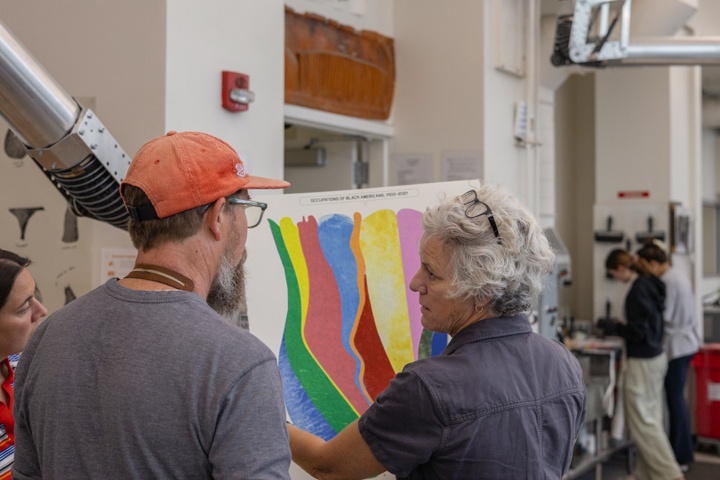 Artist holds up a print of a colorful data visualization print to show helpers.