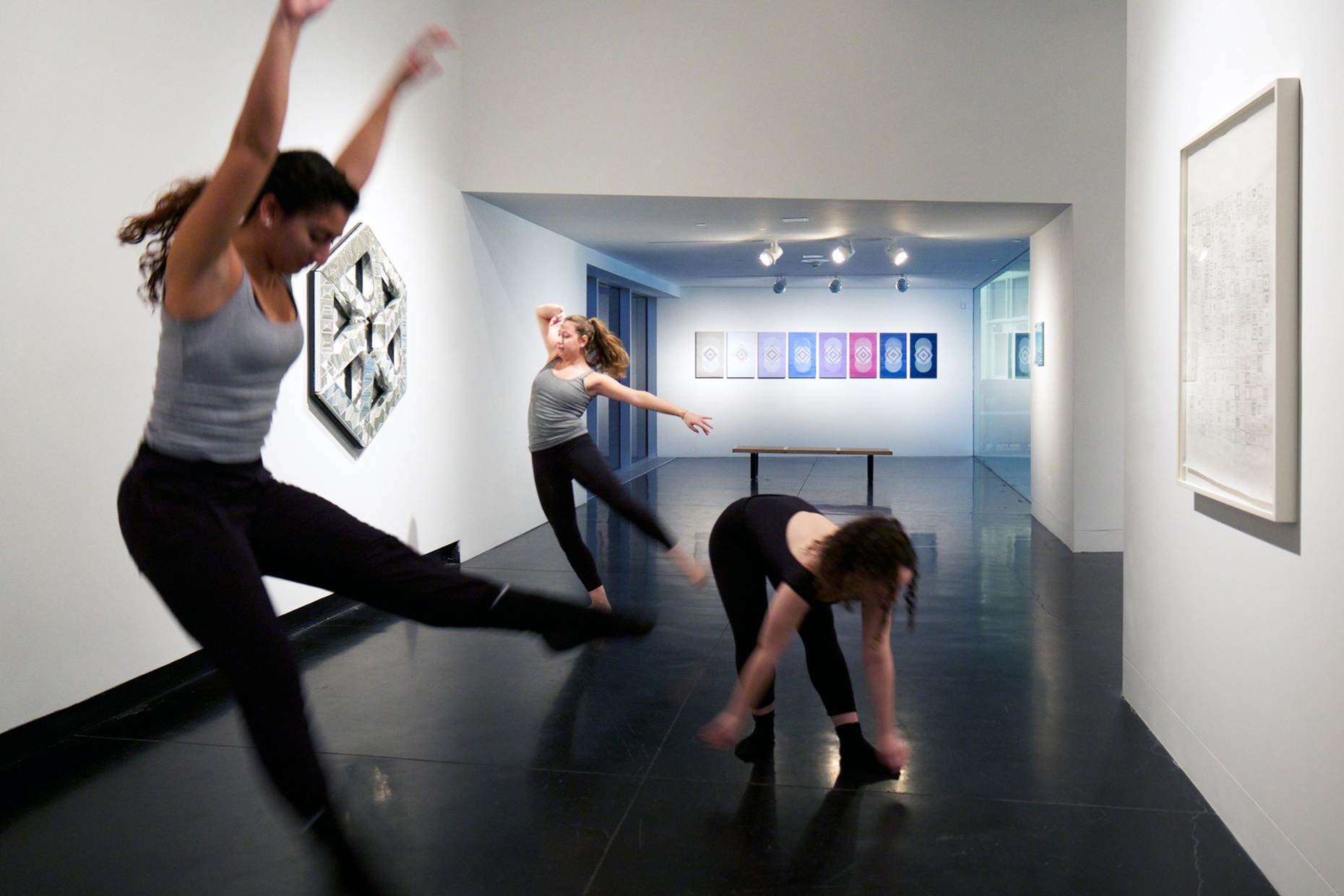 Three female, light-skinned dancers pose in a gallery space.