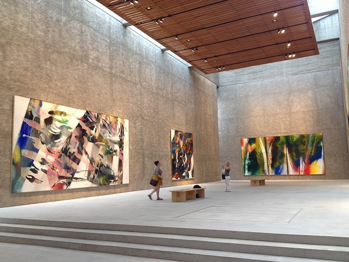 Interior of a high-ceilinged, well-lit modern gallery space with concrete walls and floor displaying large-scale abstract paintings.
