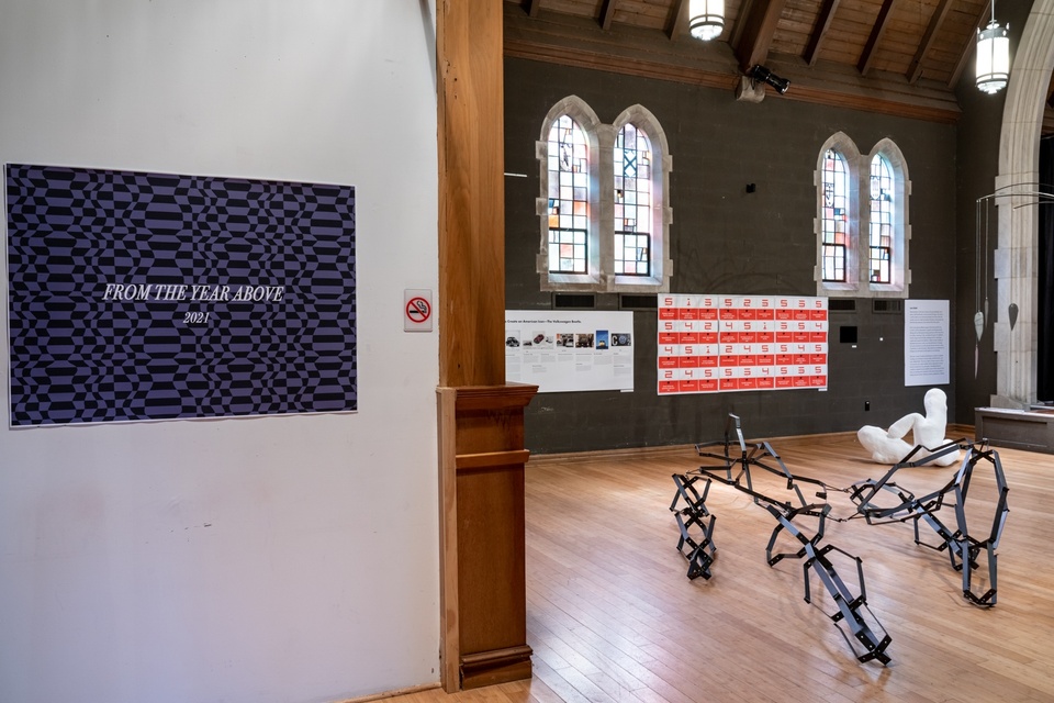 Chapel space with stained glass windows with several artworks displayed. Wall label reads "From the Year Above 2021."