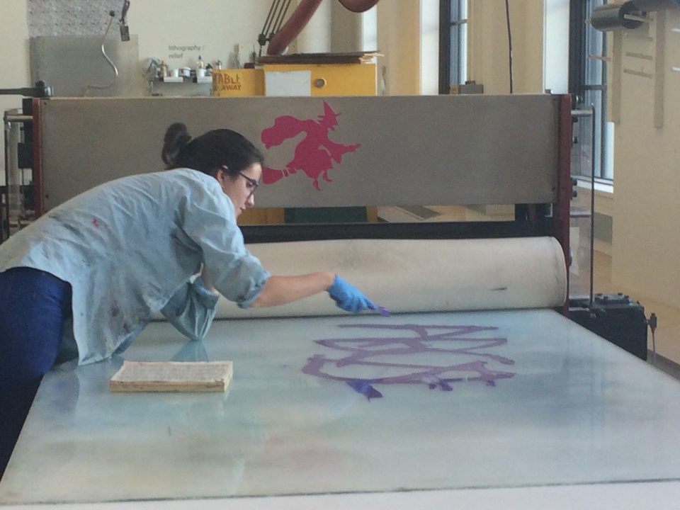 A student bent over a glass panel with a paintbrush working on a print