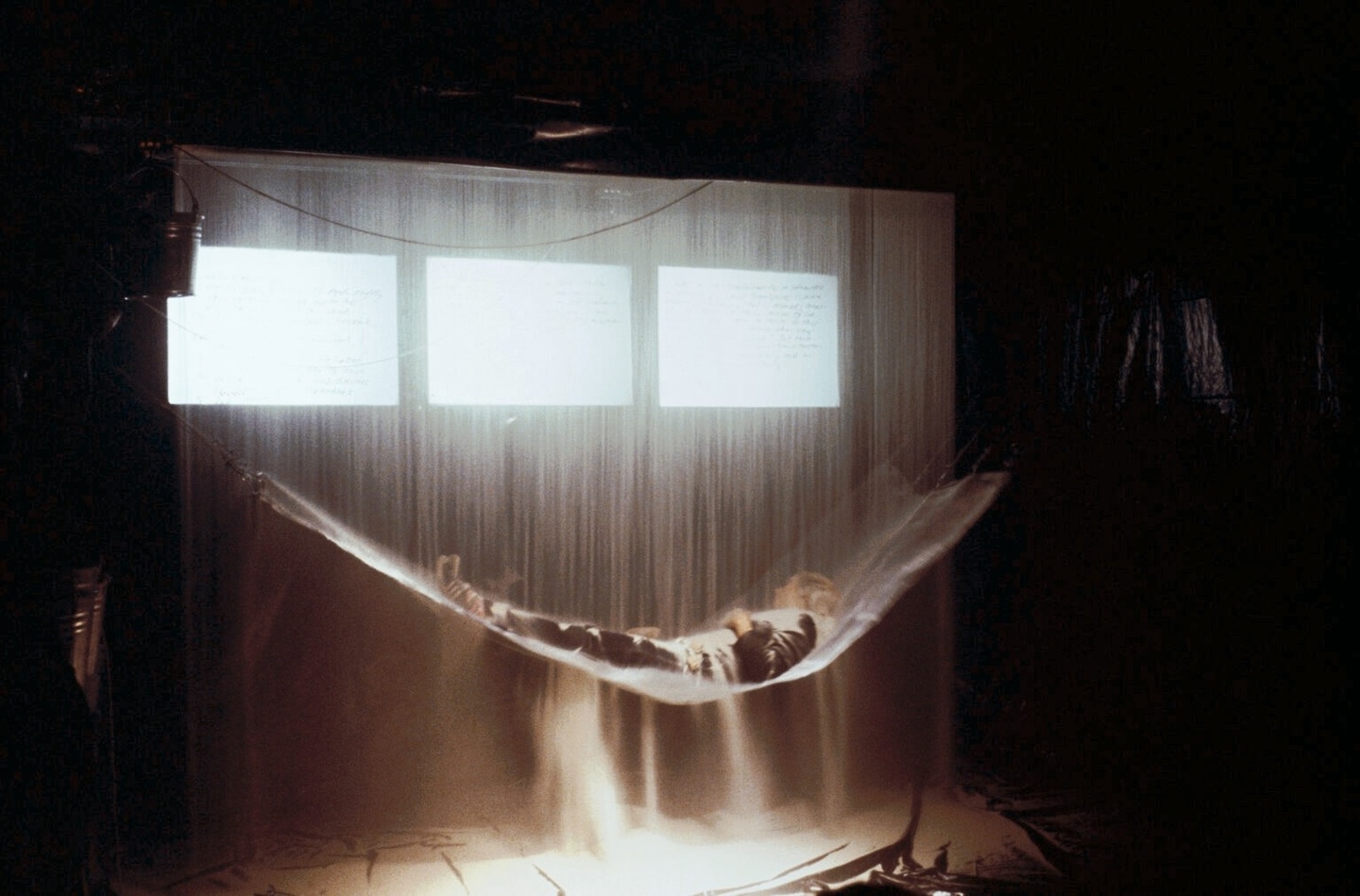 a person laying in a hammock in a dark room in front of a window with light streaming over them