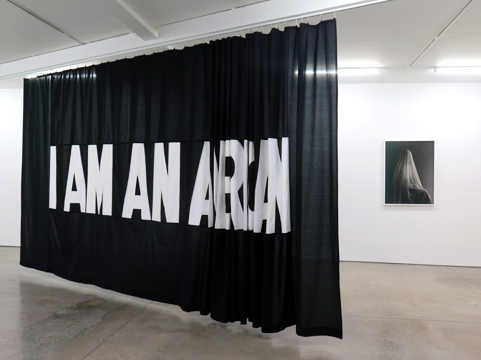 A large, black, fabric banner hanging from the ceiling with white, printed text, "I AM AN AMERICAN."