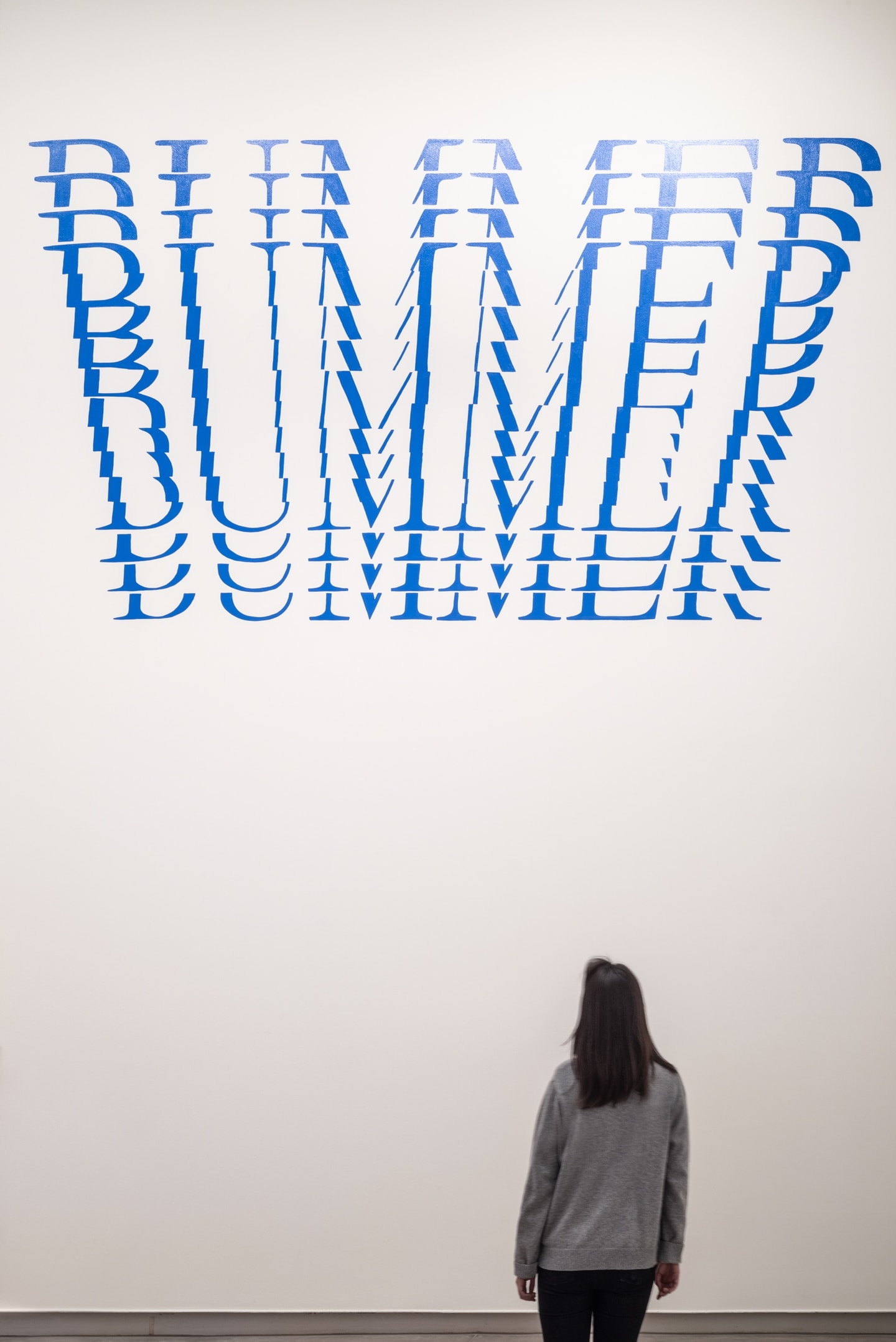 Large blue text on the gallery wall with the word BUMMER repeated in horizontal cutouts