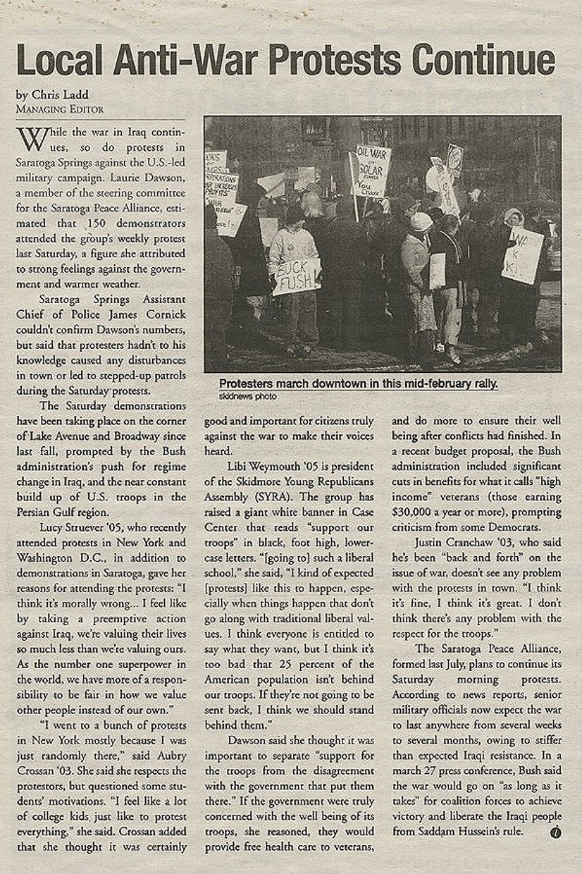 A yellowed newspaper article with a black and white photograph of people holding signs standing on a street corner with text and the headline "Local Anti-War Protests Continue."