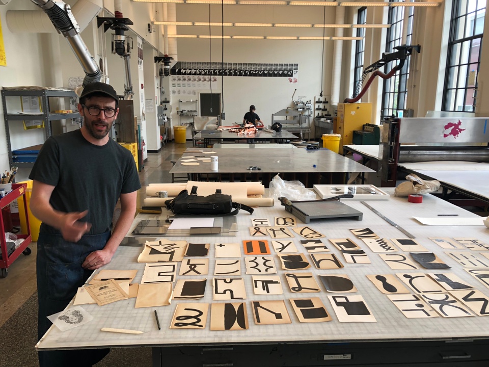 Artist standing in print shop next to his drawings on the table.